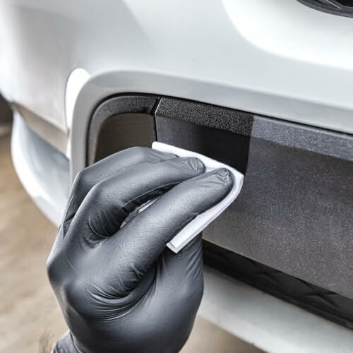 Person cleaning car bumper with cloth and wearing black gloves