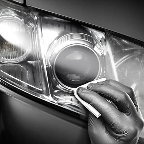 Hand cleaning a car headlight with a cloth.