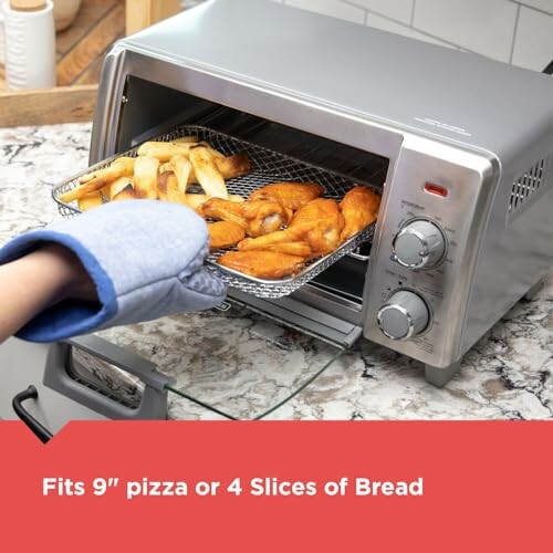 Hand with glove using compact toaster oven with food inside.
