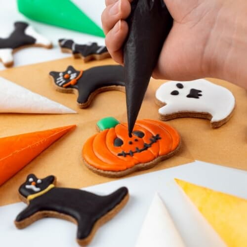 Hand decorating Halloween cookies with icing, featuring pumpkin, cat, and ghost designs.