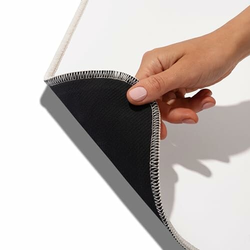 Hand holding the corner of a fabric piece with stitched edges.