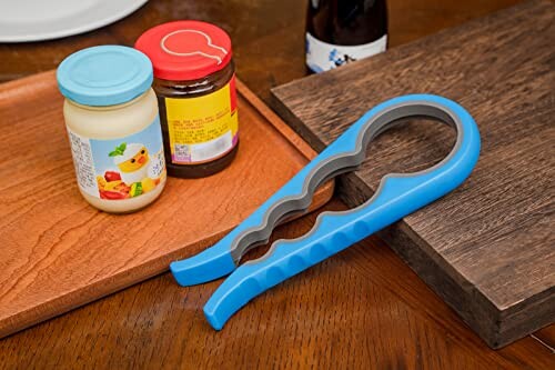 Blue jar opener next to mayonnaise and jam jars on a wooden surface.
