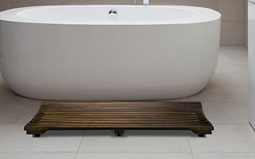 Modern white bathtub with wooden bath mat.