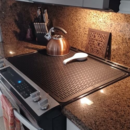 Modern kitchen stove with a kettle and utensil on a grill surface.