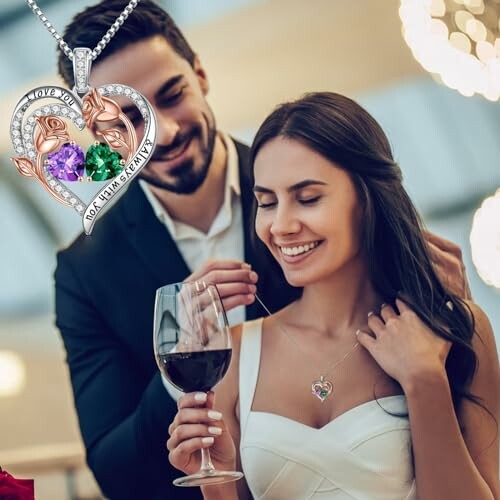 Smiling couple, woman receiving heart-shaped necklace, holding wine glass.