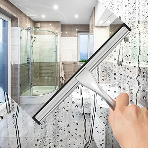 Hand using squeegee to clean glass shower door with water droplets