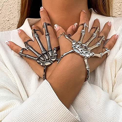 Person wearing skeleton hand jewelry over a white sweater.