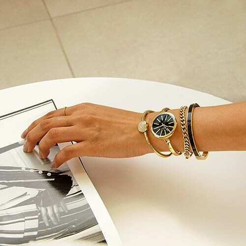 Hand wearing a watch and gold bracelets on a table