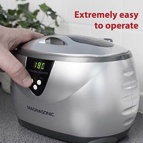 Person using a Magnasonic ultrasonic cleaner with display showing 180, labeled extremely easy to operate.