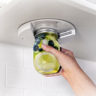 Hand using an under-cabinet jar opener with a jar of fruit-infused water.