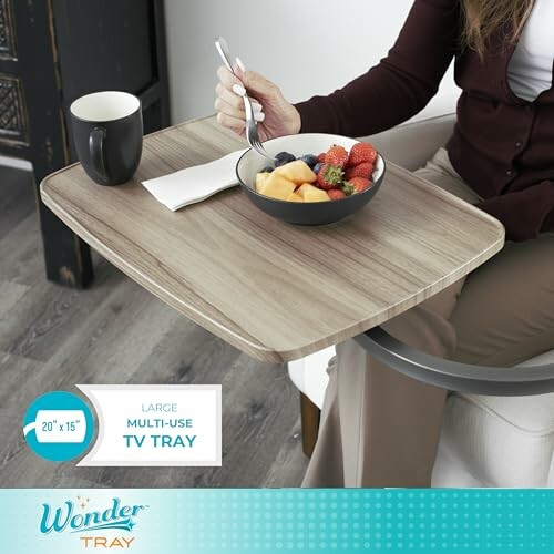 Person using a wooden TV tray with a bowl of fruit and a mug.