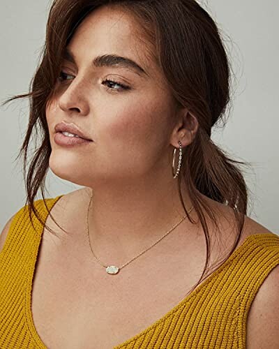 Woman wearing a yellow top with a necklace and hoop earrings.